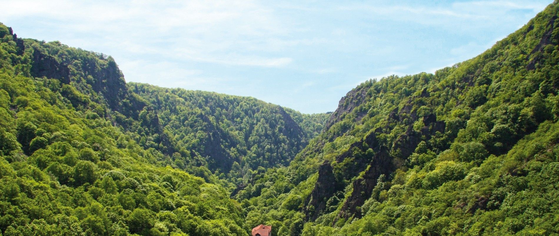 Eine malerische Berglandschaft mit grünen bewaldeten Hügeln und einem roten Dach eines Gebäudes im Vordergrund.