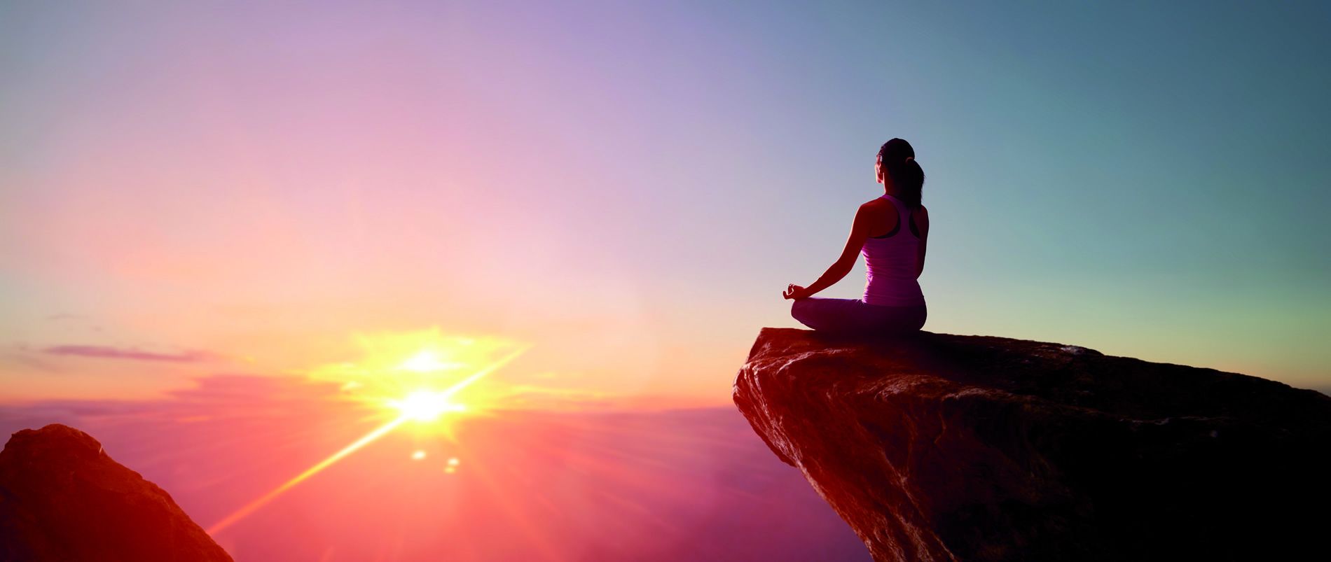 Eine Person meditiert auf einem Felsen bei Sonnenuntergang