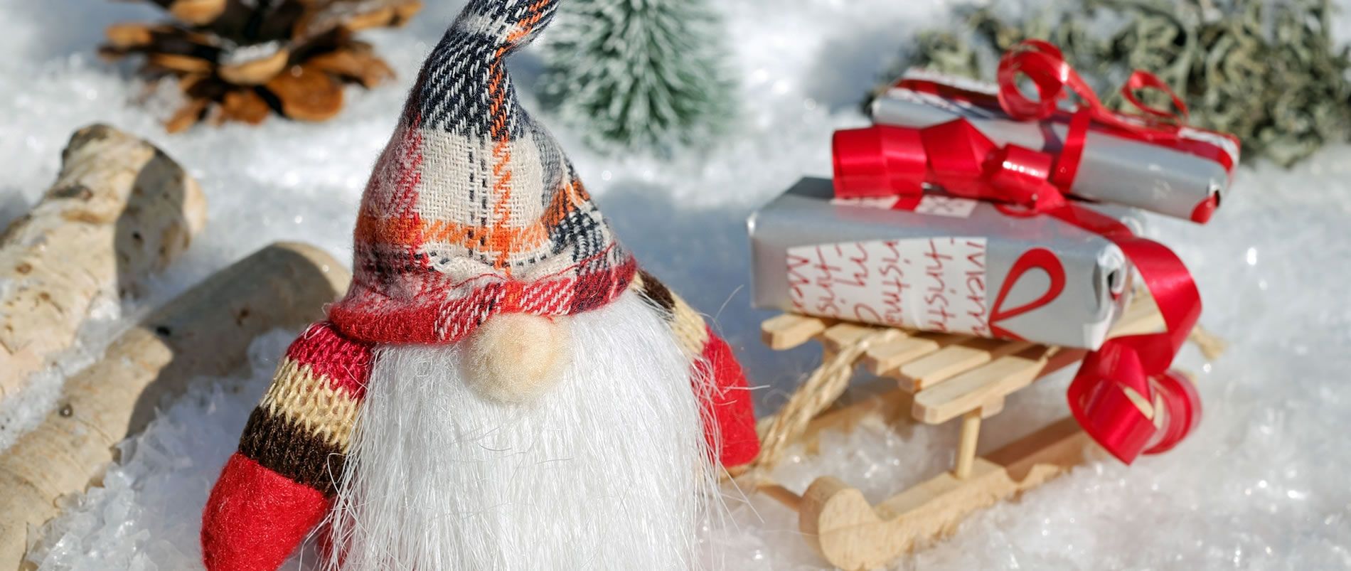 Dekorativer Weihnachtswichtel und Geschenke auf einem Schlitten im Schnee.