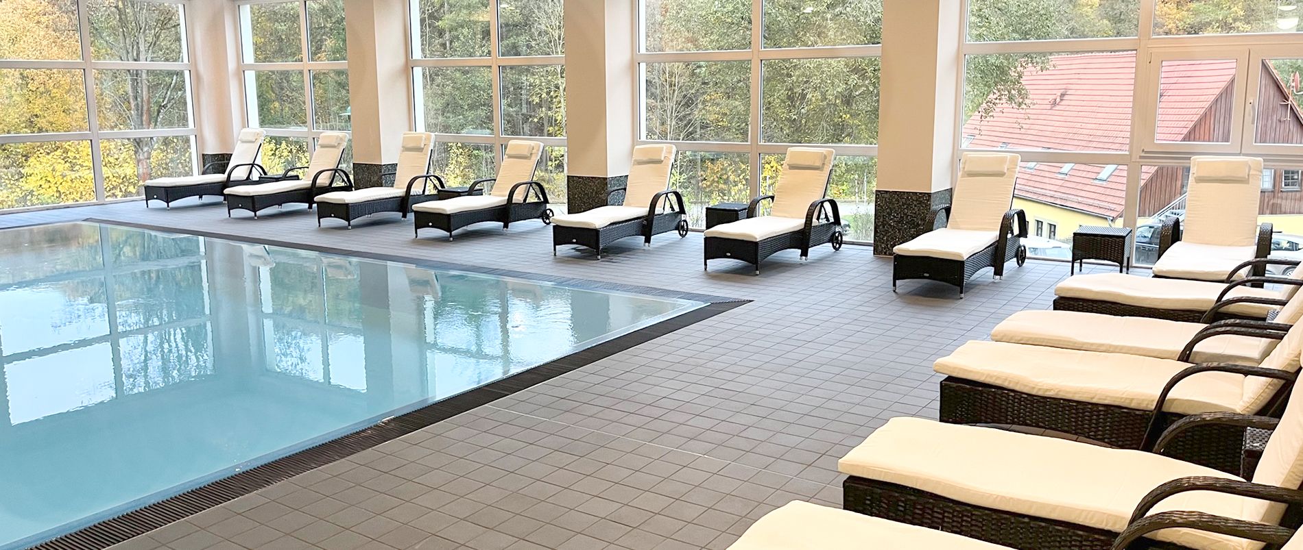 Innenansicht eines Wellnessbereichs mit Pool und gepolsterten Liegestühlen.