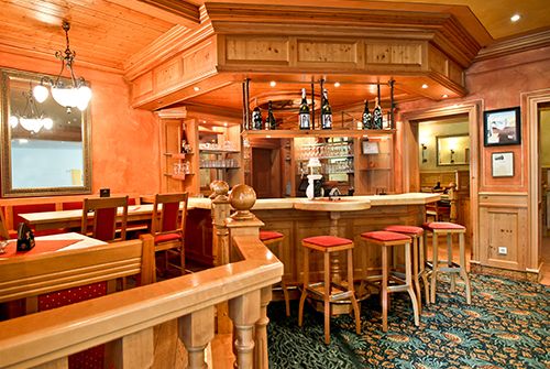 Gemütliche Bar mit Holzeinrichtung, Spiegelwand und Barhockern.