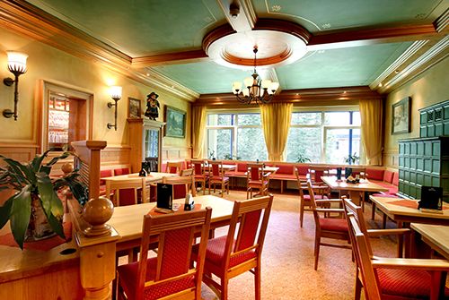 Gemütlicher Gastraum mit Holzmöbeln, roten gepolsterten Bänken und Stühlen, großen Fenstern und grüner Decke.