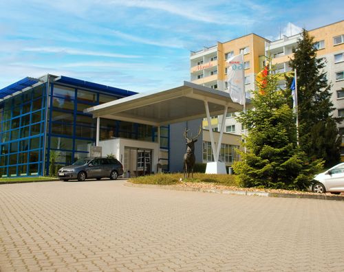 Eingangsbereich eines modernen Gebäudes mit Glasfront, einem Auto und einer Hirschskulptur