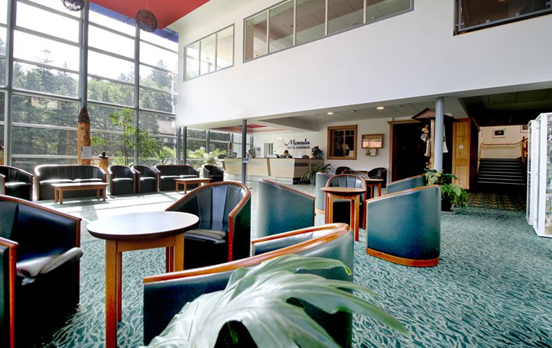 Heller Eingangsbereich mit Sitzgelegenheiten, großen Fenstern und Rezeption im Hintergrund.