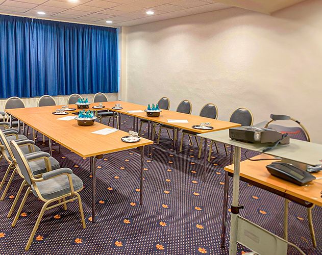 Ein Konferenzraum mit U-förmig angeordneten Tischen, bereit für ein Meeting, mit Mineralwasser, Gläsern und Notizblättern.