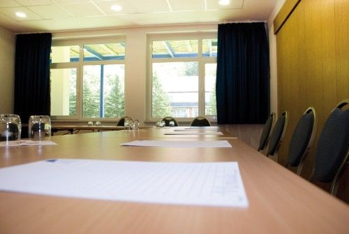 Leerer Konferenzraum mit Tisch, Stühlen, Wassergläsern und Notizblättern.
