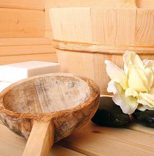 Holzeimer und Kelle mit einer weißen Blume und schwarzen Steinen auf einem Holztisch.