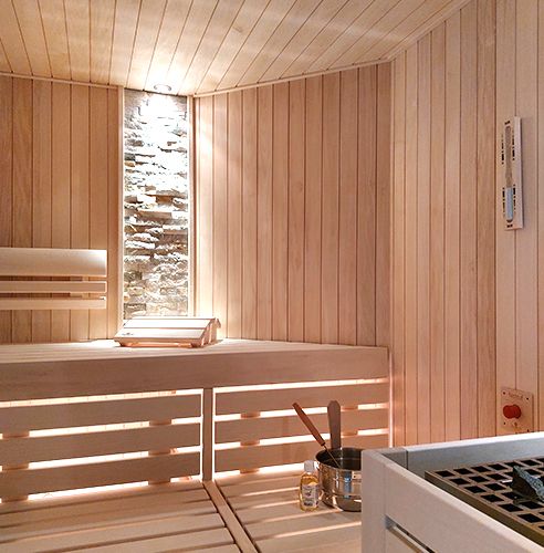 Innenansicht einer modernen Sauna mit Holzbänken, einem Steinwandabschnitt und einem Saunazubehör-Set.