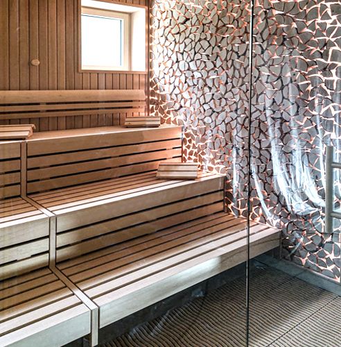 Moderne Sauna mit hellen Holzbänken und dekorativer Wand.