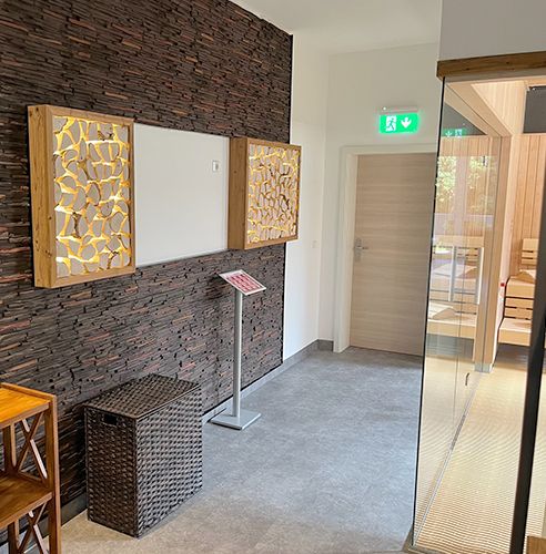 Moderner Eingangsbereich mit Holzakzentwand, dekorativen Leuchten und Glastür zu einer Sauna.