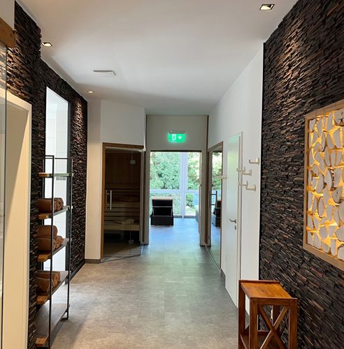 Flur mit dunkler Steinwand in einem modernen Interieur, mit Handtüchern auf einem Regal und einer Sauna im Hintergrund.