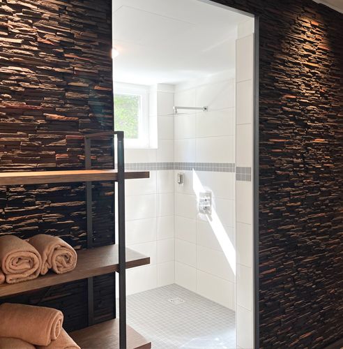 Moderner Duschbereich mit weißen Fliesen, einem kleinen Fenster und angrenzendem Regal mit gefalteten Handtüchern.