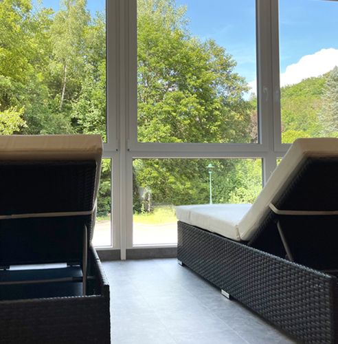 Zwei Liegen vor einer großen Glasfront mit Blick auf grüne Bäume.