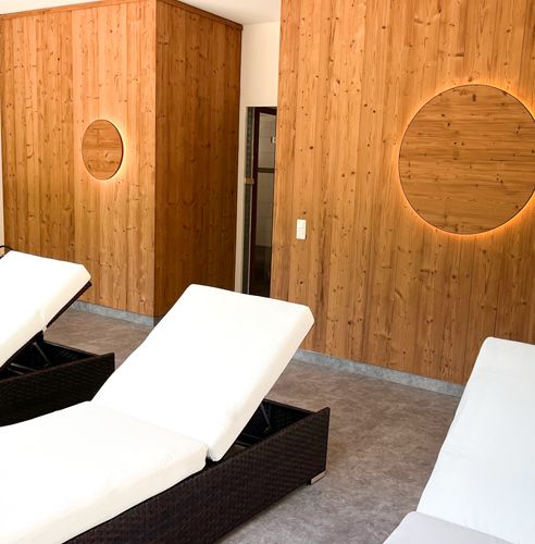 Entspannungsraum mit Holzwänden und weißen Liegestühlen