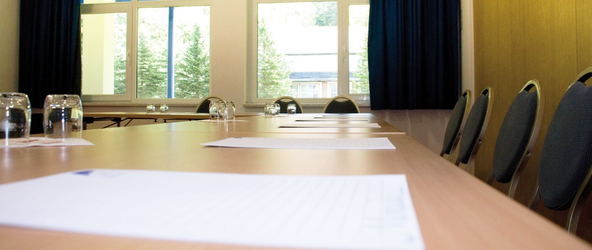 Leerer Konferenzraum mit einem großen Tisch, umgeben von Stühlen und einem Notizblock und Gläsern auf dem Tisch.
